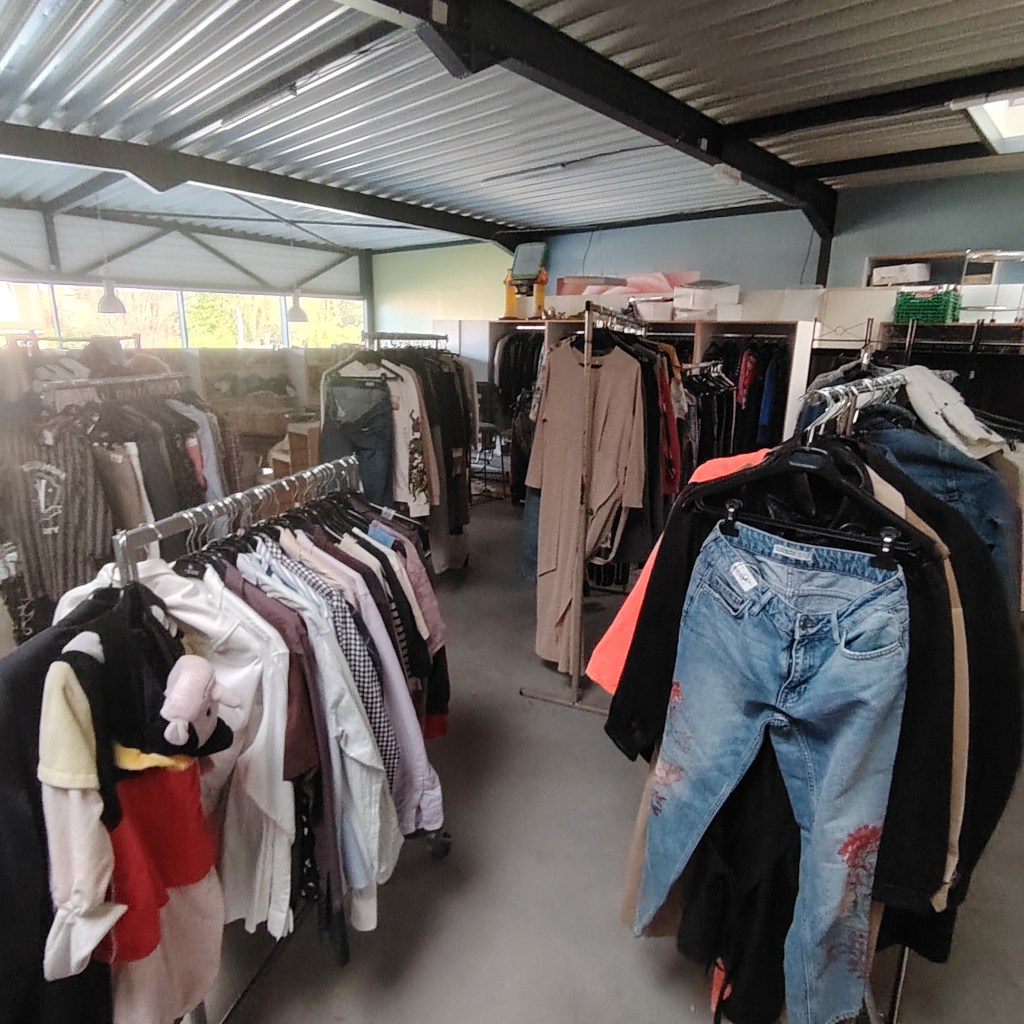 Intérieur d'une boutique de seconde main avec des vêtements exposés sur des portants, montrant une variété d'articles pour toute la famille.